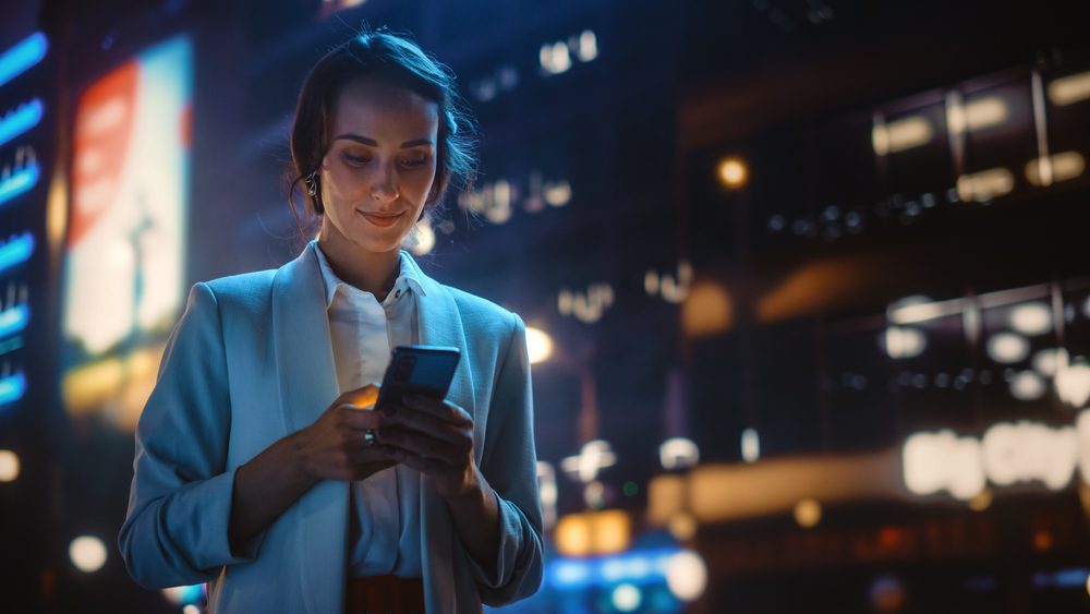 Beautiful,Young,Woman,Using,Smartphone,Walking,Through,Night,City,Street